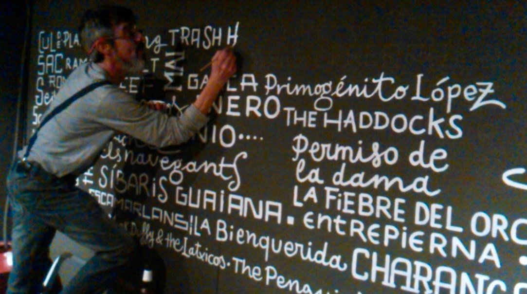 David Molins pintant a mà els noms dels grups i cantants al mur del Milenio
